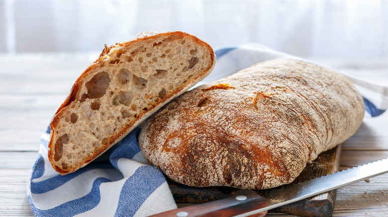 Loaves of ciabatta on a wooden board with a bread knife and kitchen towel