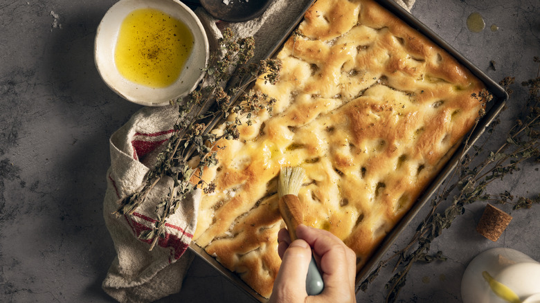 Tray of focaccia being brushed with olive oil