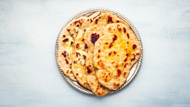 Round metal dish with several naans stacked on it