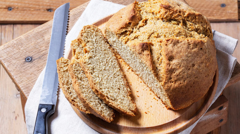 Whole loaf of soda bread on a cutting board with a bread knife and three cut slices