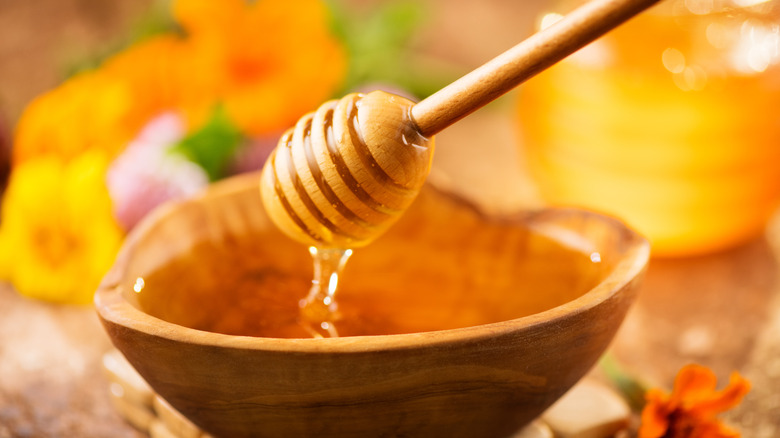 A honey dipper dripping honey into a wooden bowl 