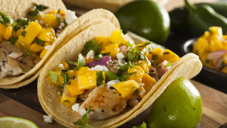 Two Baja fish tacos topped with mango and cilantro with a lime garnish