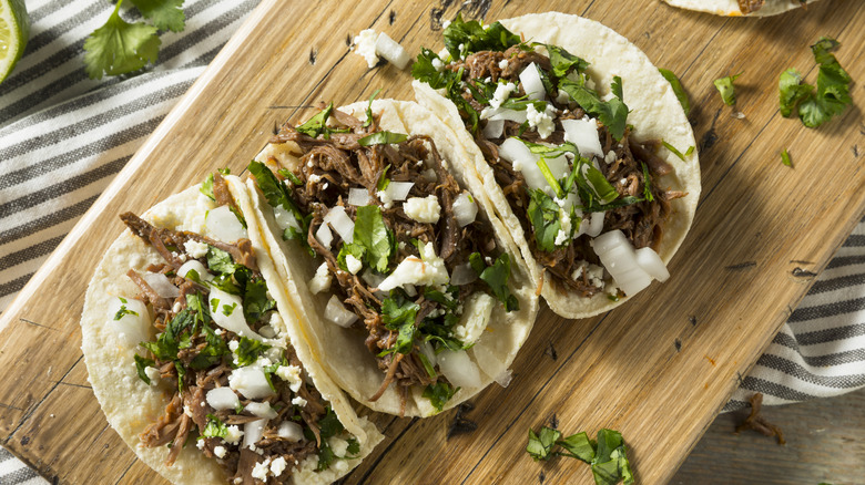 Home made beef barbacoa tacos with cilantro and onion on a wooden board