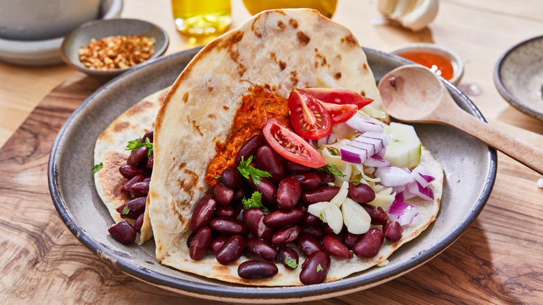 Two bean tacos topped with tomato onion and cilantro on a pottery place that is placed on a wooden board. Various dishes in the background.