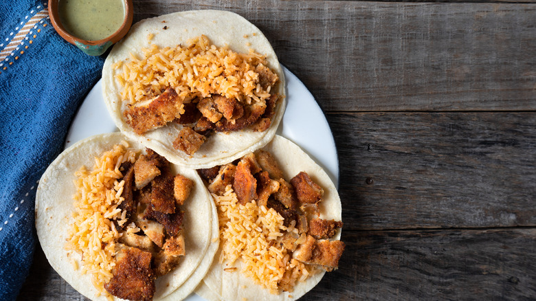 Milanesa tacos with red rice served on a wooden background with a blue cloth and a pot of sauce