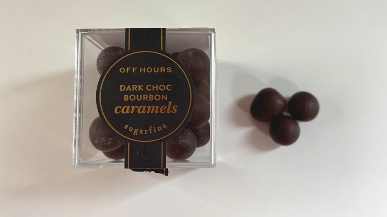 Box of Sugarfina dark chocolate caramels next to three chocolate caramels on white table