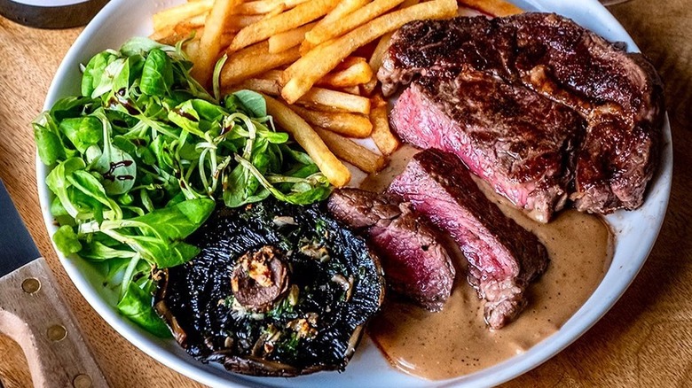 Plate of steak and chips with grilled mushroom, salad, and peppercorn sauce