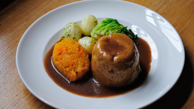 Plate of steak and kidney pudding with potatoes and vegetables