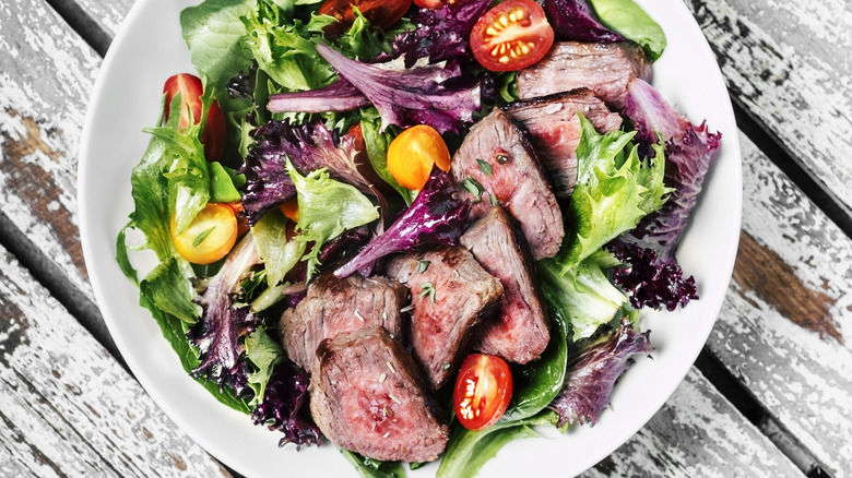 Plate of steak salad with greens and sliced tomatoes