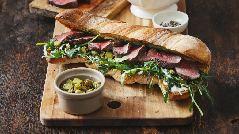 Steak sandwich with arugula and pickles in crusty bread