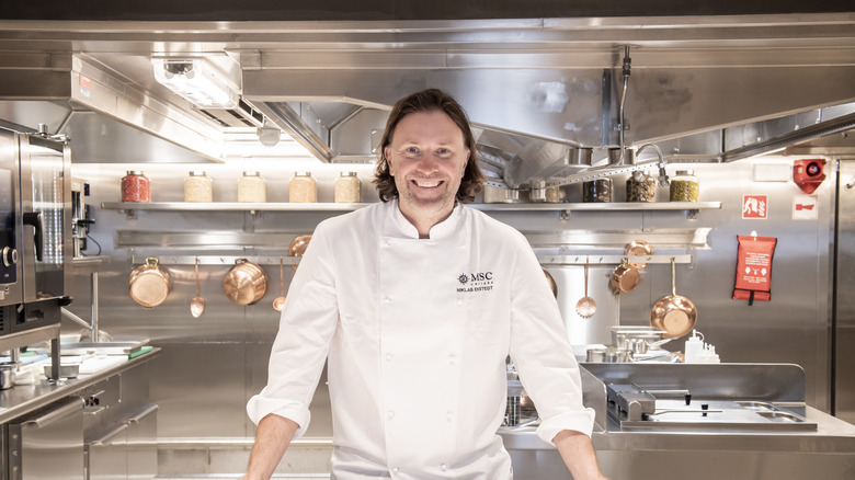 A cruise ship chef smiling at the camera lens in a professional kitchen