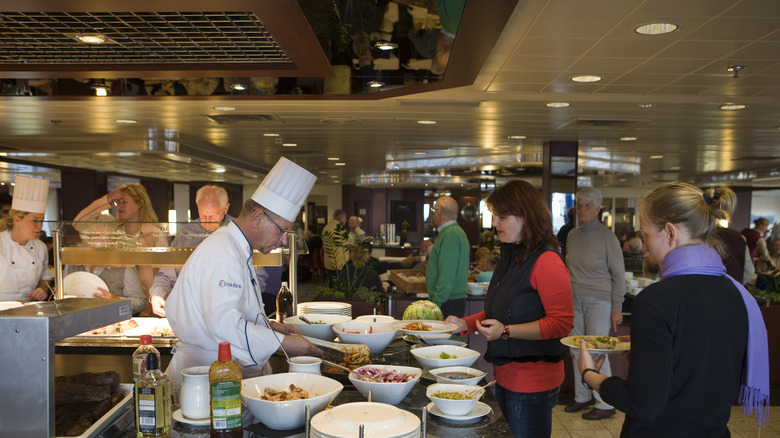 Cruise staff and guests handling food at a cruise ship buffet