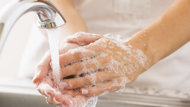 Person with soapy hands washing hands under running water at sink