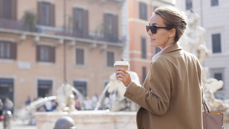 Blonde woman in Italy standing with a to-go coffee cup and a handbag