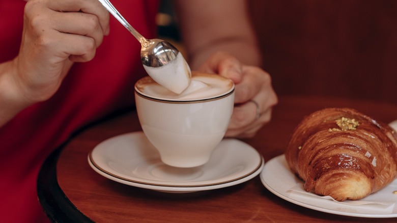 Foamy milk being pulled up with a spoon out of a white ceramic cup