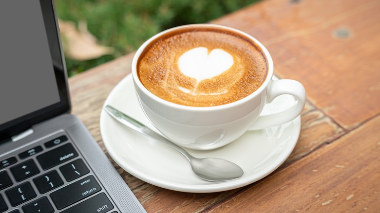 A toasted latte with a foam heart on top next to a laptop