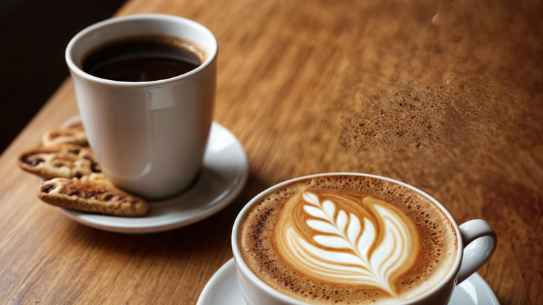 A cup of espresso and a latte with foam art on a table