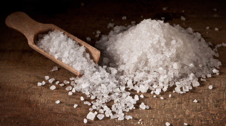 Pile of rock salt and salt shovel on wooden surface