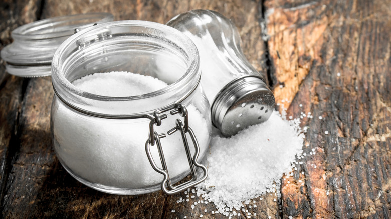 Open jar of salt and spilled salt next to fallen salt shaker