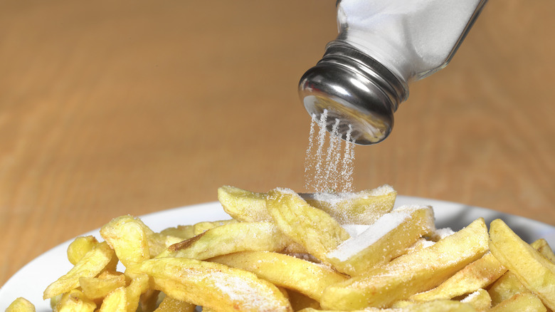 Salt from shaker being added to plate of fries