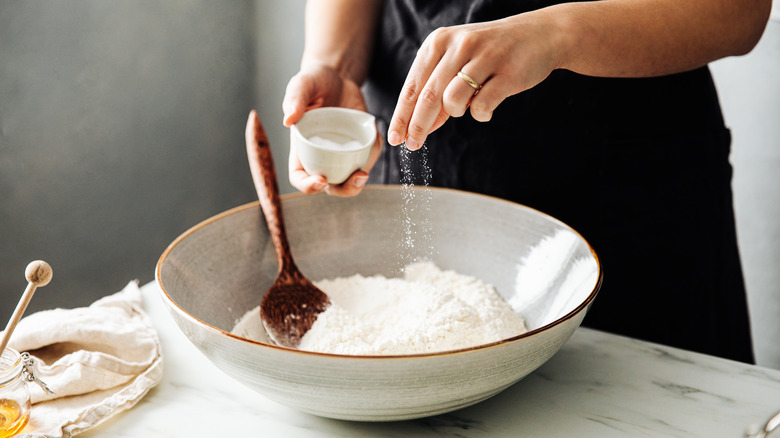 Person adding salt into bowl of flour