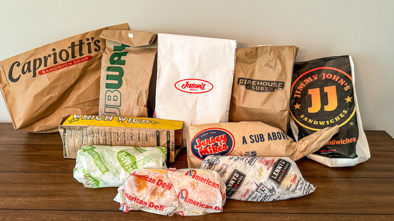 Selection of deli sandwiches in brown bags and parchment paper