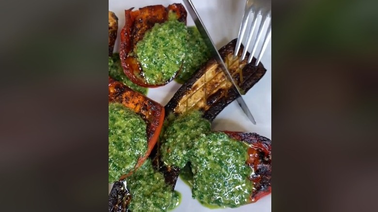 Cutting pesto-topped grilled vegetables with knife and fork