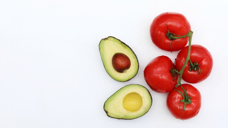 avocado halved next to bunch of tomatoes