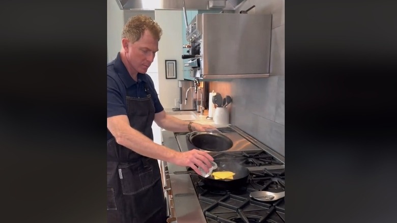 Chef Bobby Flay adding water to a pan whilst frying a cheese burger