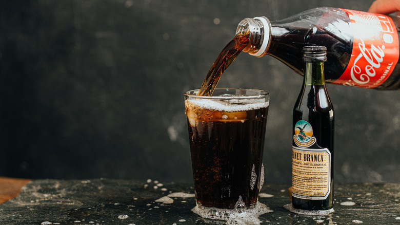 Fernet and coke being poured into a glass tumbler