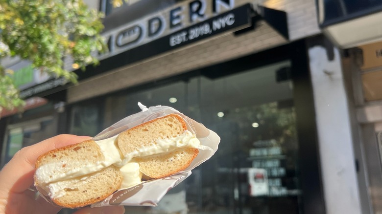 A Modern Bread and Bagel gluten-free cream cheese bagel is held in front of the store.