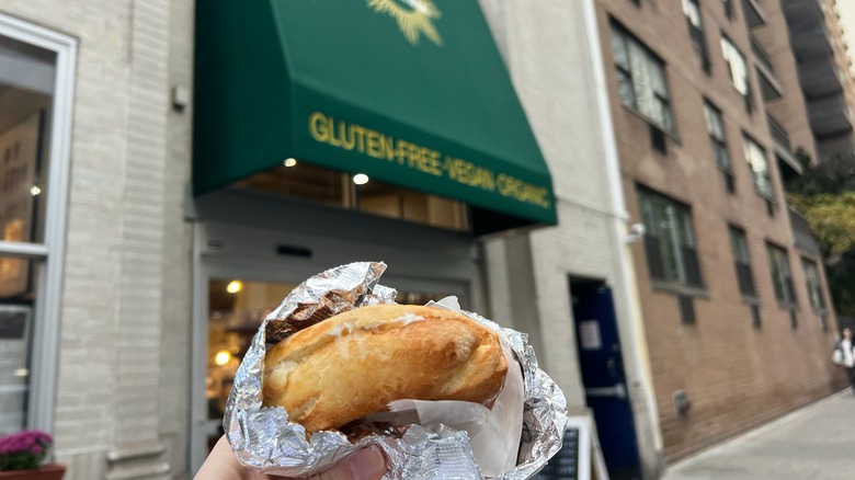 An Agata & Valentina gluten-free cream cheese bagel is held in front of the store.