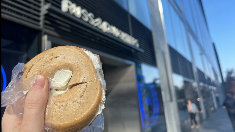 A Russ & Daughters gluten-free cream cheese bagel is held in front of the store.