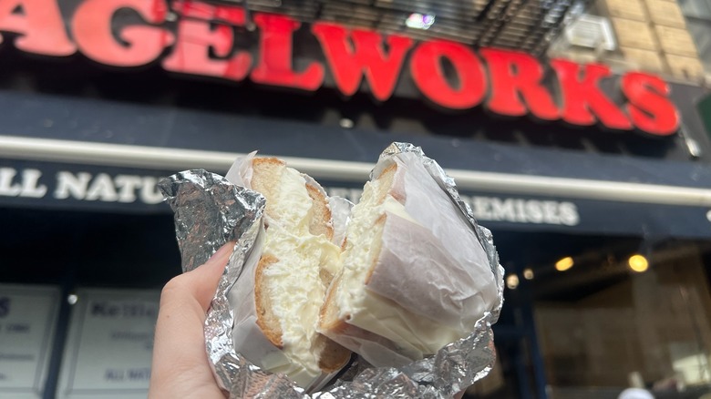 A Bagelworks gluten-free cream cheese bagel is held in front of the store.