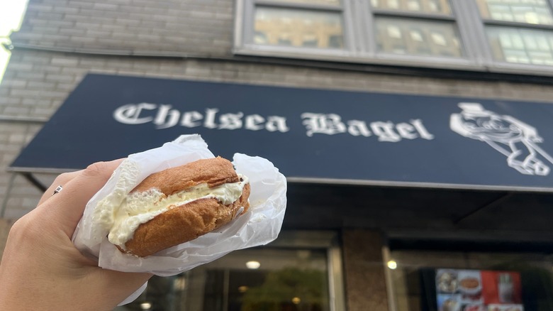 A Chelsea Bagel gluten-free cream cheese bagel is held in front of the store.