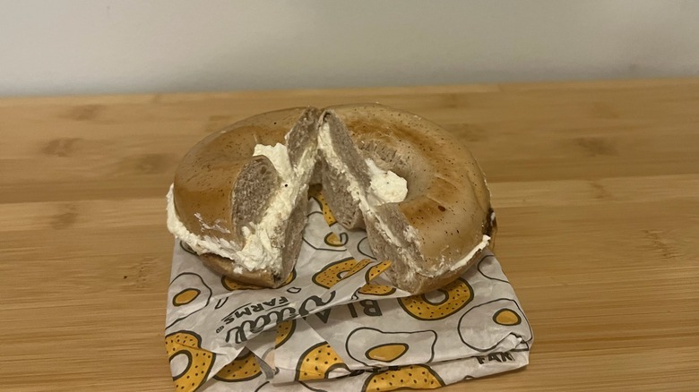 A cream cheese gluten-free bagel is sitting on a wooden table.