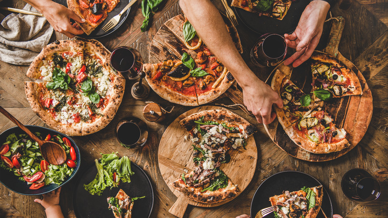 people grabbing pizza with wine