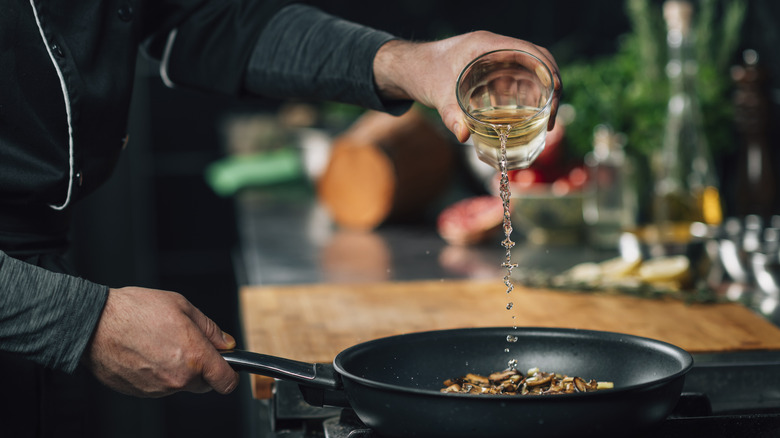 Chef pouring white wine into a frying pan with sliced shiitake mushrooms