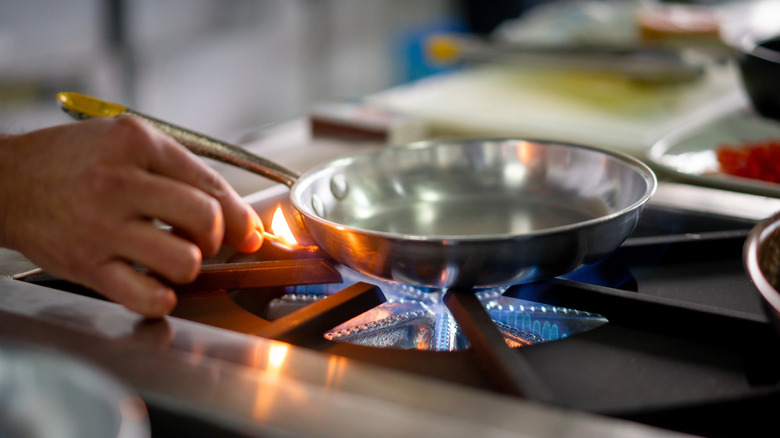 Close-up on a chef lighting up a gas stove burner with a match while working at a restaurant