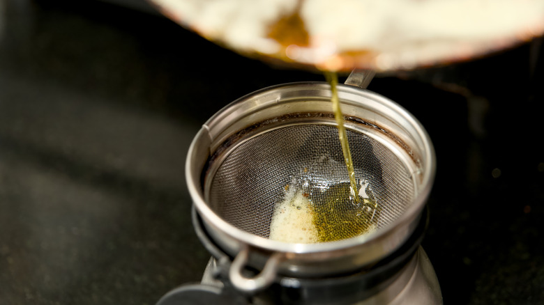 Golden clarified fat being carefully strained through a sieve