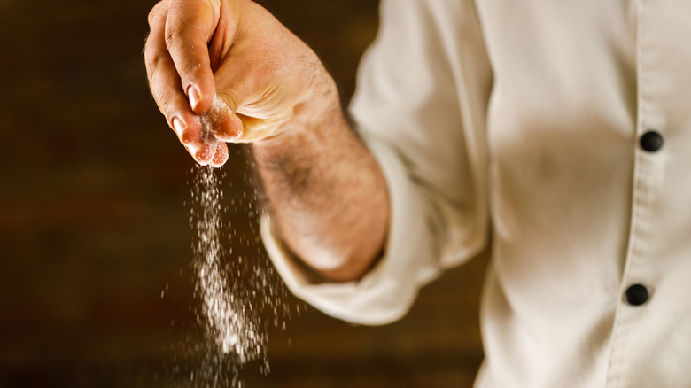 Close up of unrecognizable chef adding salt while preparing a meal in the kitchen