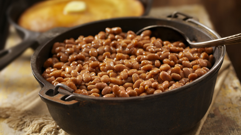 A cast iron bowl of baked beans with spoon in it