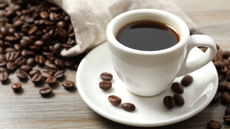 A mug of black coffee surrounded by coffee beans