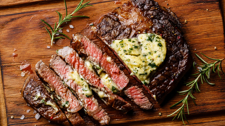 Seared steak sliced and topped with herb butter on chopping board