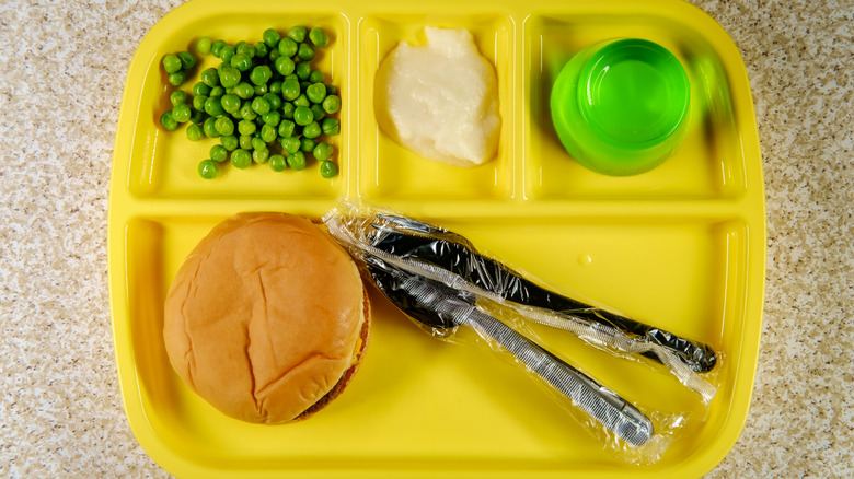 school lunch tray with cheeseburger, peas, mashed potatoes and green jello