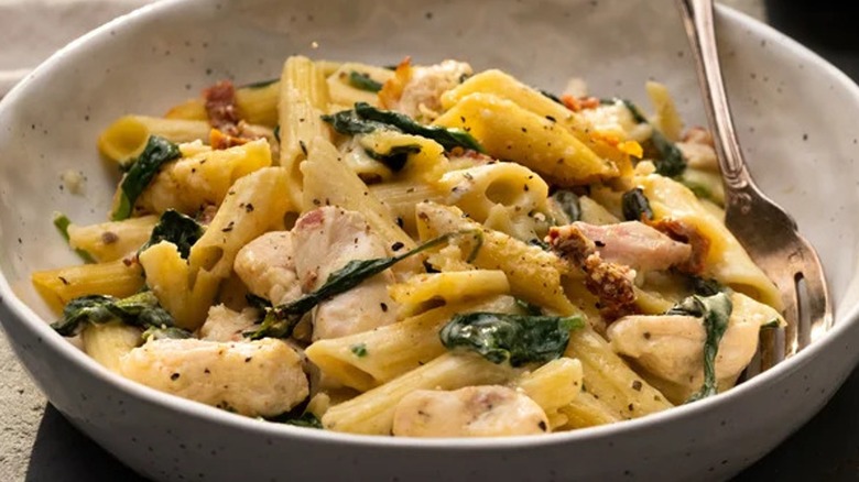 Close-up of a bowl of chicken and spinach penne with a fork 