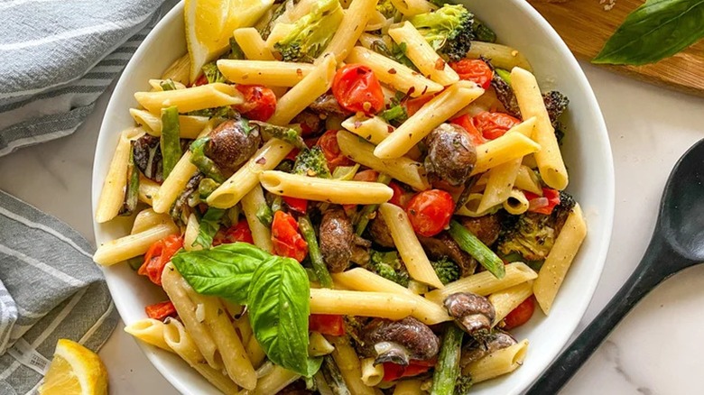 Top-down view of a bowl of vegetable penne next to a spoon