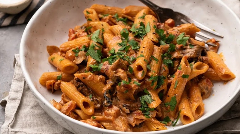 A bowl of penne boscaiola with an herb garnish