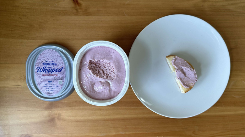 Whipped mixed berry cream cheese shown on bagel and in container.