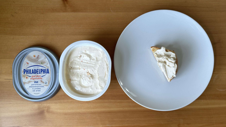 Garden vegetable cream cheese is shown on a bagel and in the container.